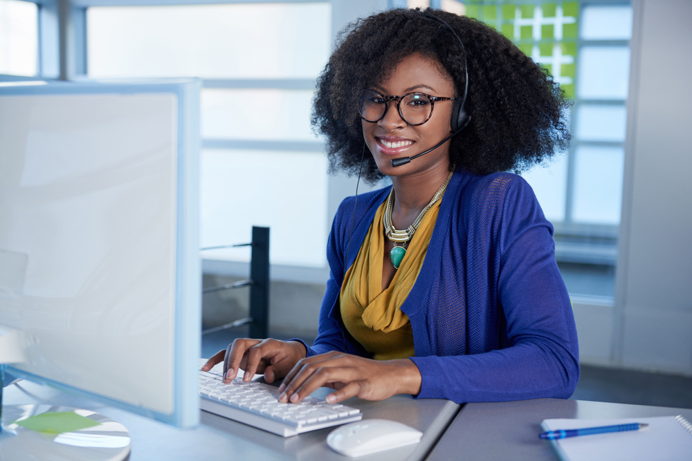 Portrait of a smiling customer service representative with an afro at the computer using headset-1